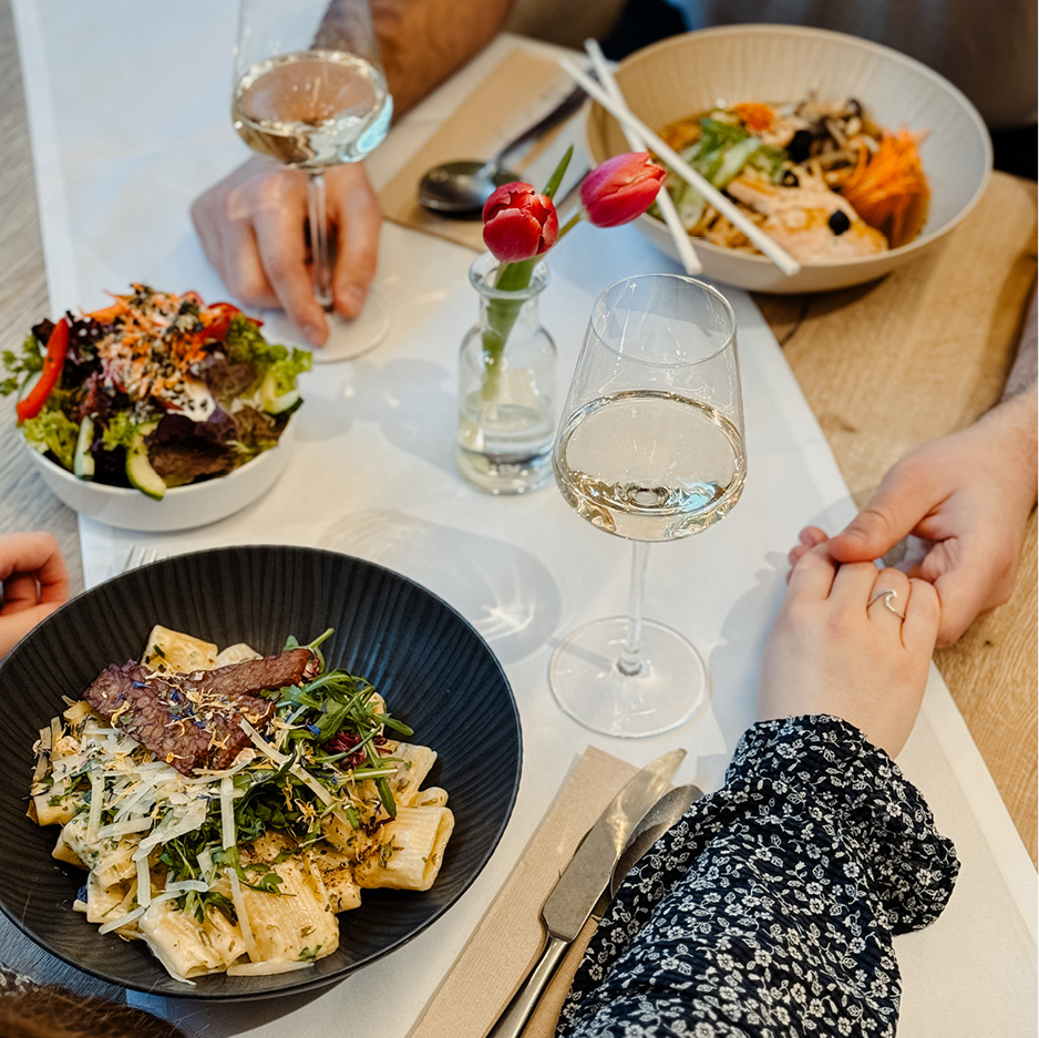 Das Bild zeigt ein Paar beim Abendessen, das über den gedeckten Tisch Händchen hält.