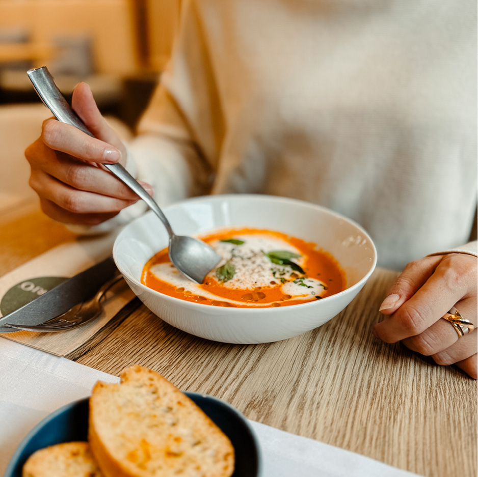 Das Bild zeigt eine cremige Suppe, in der eine Person rührt. Daneben ist ein Teller mit getoastetem Brot zu sehen.