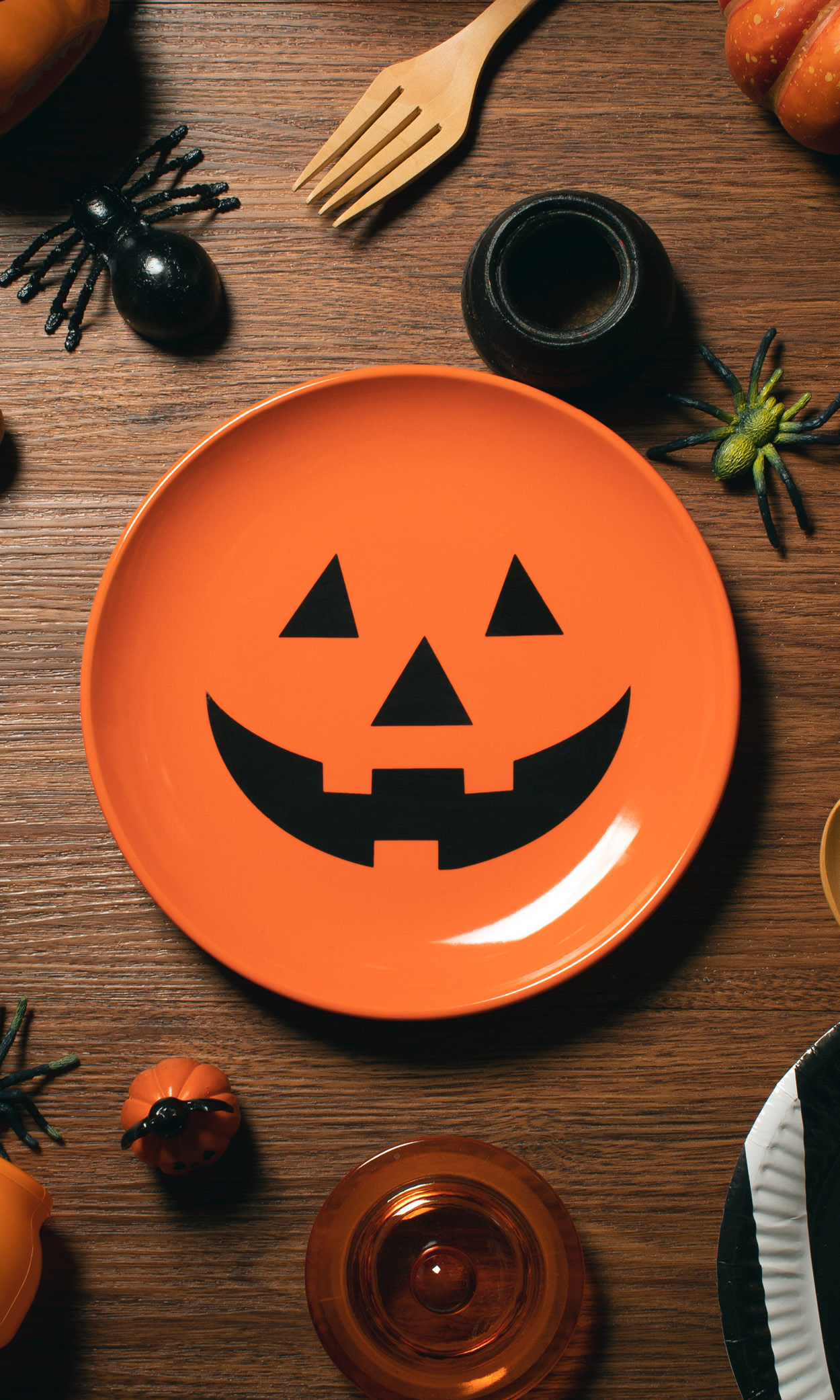 Das Bild zeigt einen orangen Teller mit Grimasse rund um Halloween-Snacks.